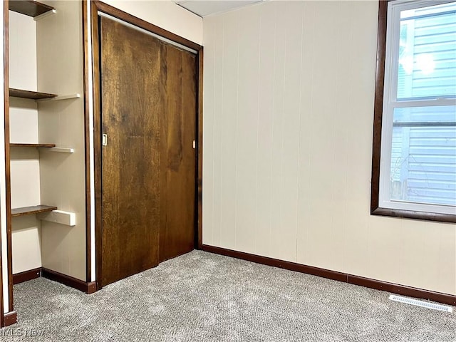 unfurnished bedroom featuring carpet floors, a closet, and wooden walls