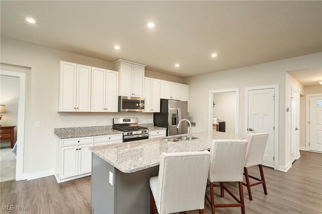 kitchen featuring white cabinets, appliances with stainless steel finishes, a kitchen bar, an island with sink, and sink