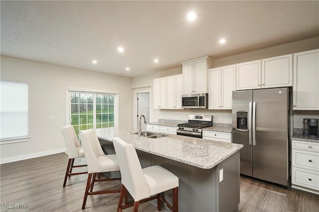 kitchen featuring a center island with sink, stainless steel appliances, a kitchen breakfast bar, white cabinets, and sink