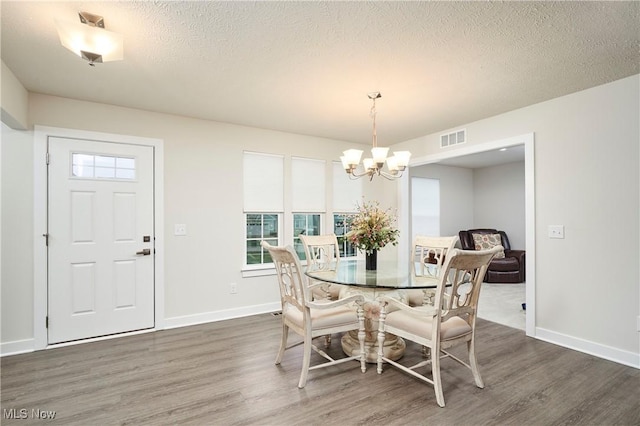 dining space with a textured ceiling, dark wood-type flooring, and a notable chandelier