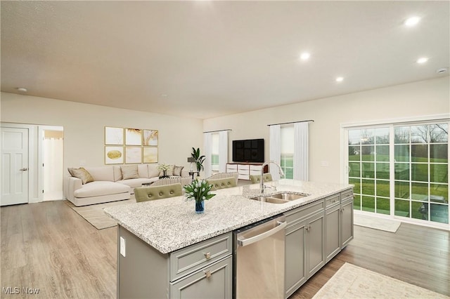 kitchen featuring light stone countertops, dishwasher, an island with sink, sink, and gray cabinetry