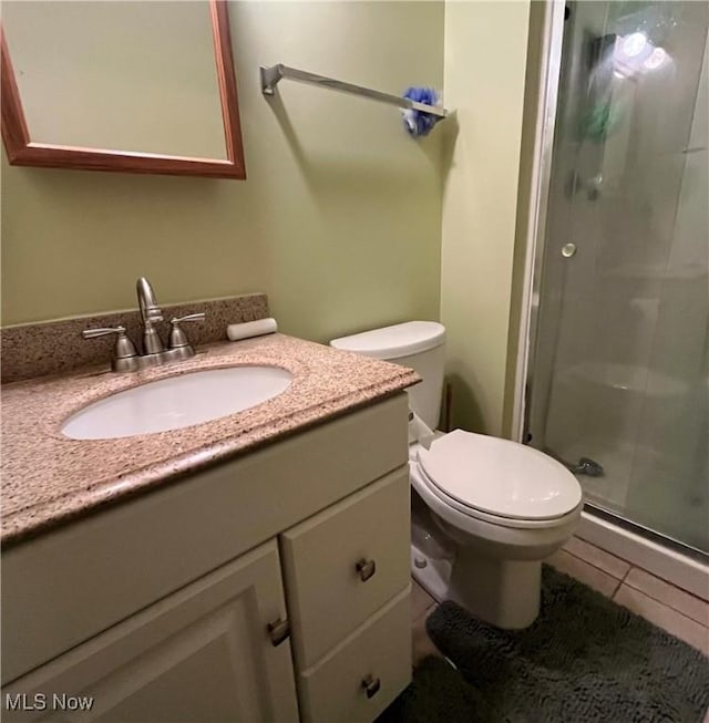 bathroom with tile patterned floors, a shower with door, vanity, and toilet