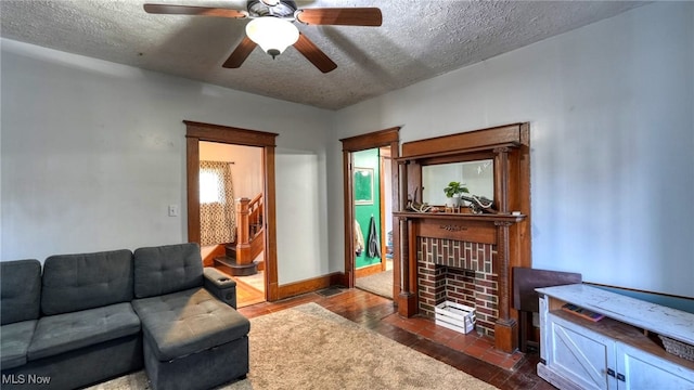 living room with ceiling fan, a textured ceiling, and a brick fireplace