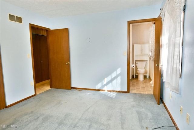 unfurnished bedroom featuring light colored carpet, a closet, and ensuite bathroom