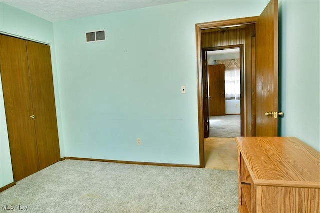 unfurnished bedroom with light carpet, a textured ceiling, and a closet