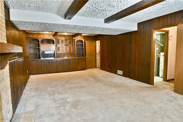 unfurnished living room with light carpet, a textured ceiling, and beamed ceiling