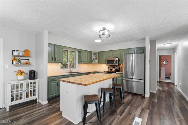 kitchen with wood counters, appliances with stainless steel finishes, a kitchen bar, dark wood-type flooring, and green cabinets