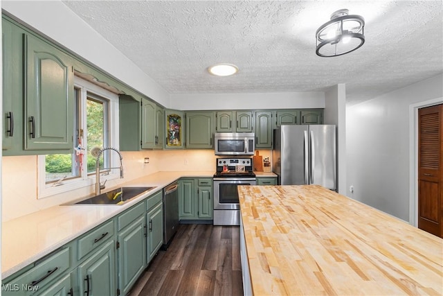 kitchen with dark wood-type flooring, green cabinets, sink, a textured ceiling, and stainless steel appliances