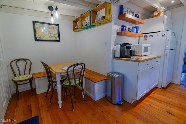 kitchen with white appliances, white cabinets, light wood-type flooring, decorative light fixtures, and beam ceiling