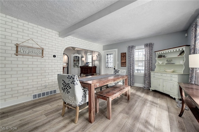 dining space featuring beam ceiling, brick wall, a textured ceiling, and hardwood / wood-style flooring