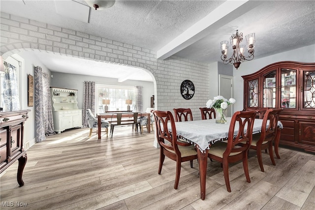 dining room with a chandelier, light hardwood / wood-style flooring, beamed ceiling, and brick wall