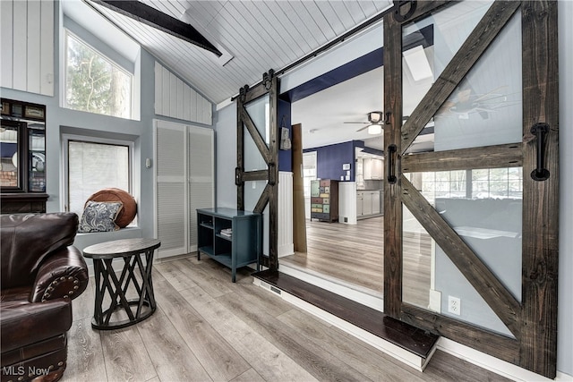 interior space featuring a barn door, vaulted ceiling, ceiling fan, and wood ceiling