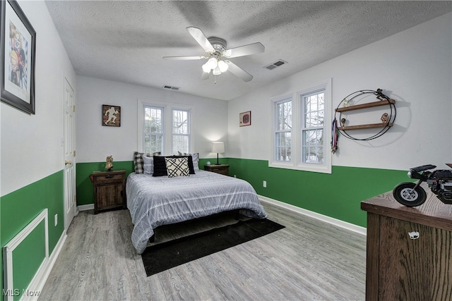 bedroom featuring ceiling fan, light hardwood / wood-style floors, a textured ceiling, and multiple windows