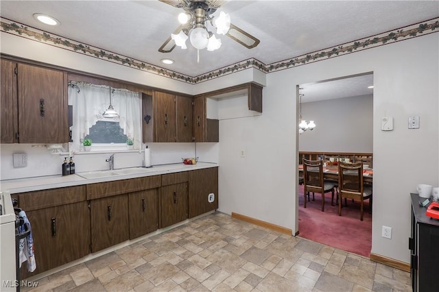 kitchen featuring ceiling fan with notable chandelier, pendant lighting, dark brown cabinetry, range, and sink