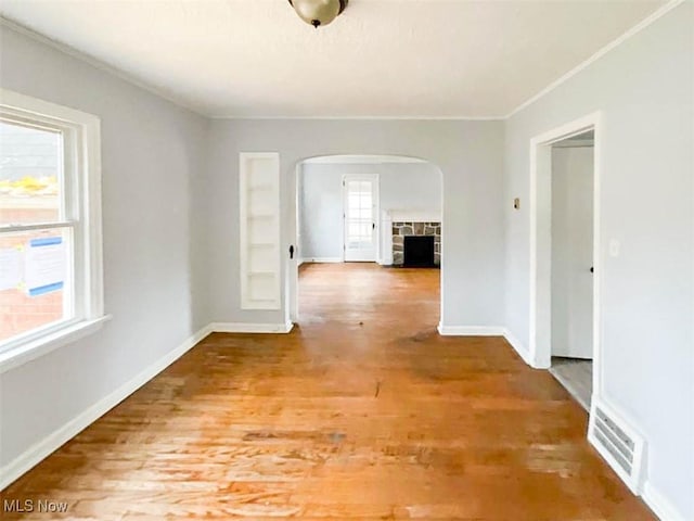 unfurnished room with a stone fireplace, a wealth of natural light, and hardwood / wood-style floors