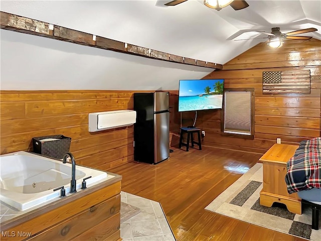 interior space featuring ceiling fan, a washtub, wood-type flooring, vaulted ceiling, and wooden walls