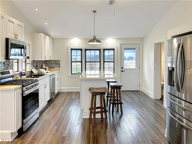 kitchen with pendant lighting, lofted ceiling, white cabinetry, and appliances with stainless steel finishes