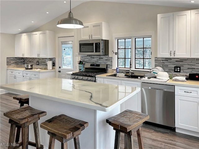 kitchen with white cabinets, appliances with stainless steel finishes, a kitchen bar, and vaulted ceiling