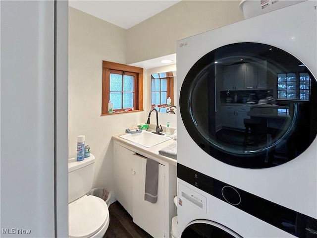 clothes washing area featuring stacked washer / dryer, dark wood-type flooring, and sink