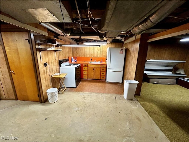 basement featuring white refrigerator, washer / dryer, sink, and wooden walls