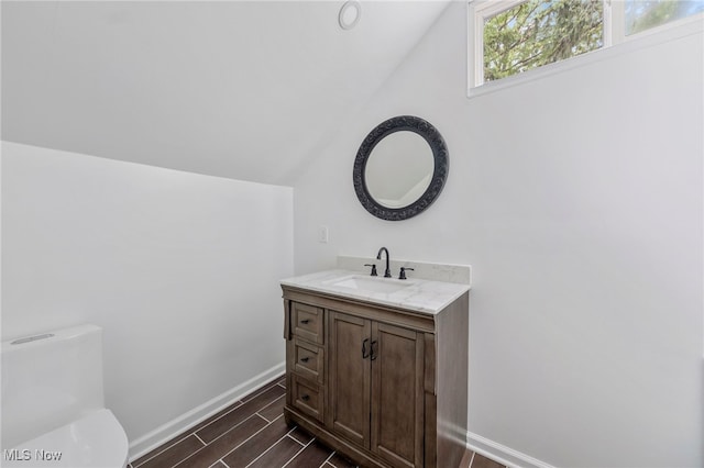 bathroom with toilet, hardwood / wood-style floors, vanity, and vaulted ceiling