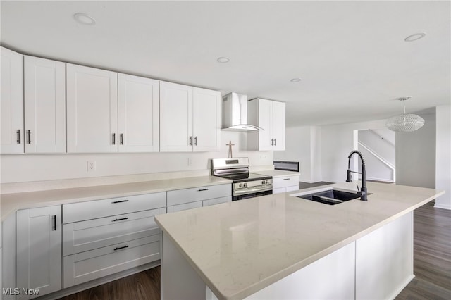 kitchen featuring dark wood-type flooring, wall chimney range hood, stainless steel range with electric cooktop, a center island with sink, and white cabinets