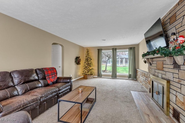 living room with a stone fireplace, light colored carpet, and a textured ceiling