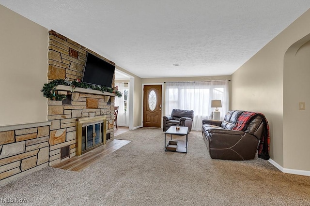 carpeted living room featuring a stone fireplace and a textured ceiling