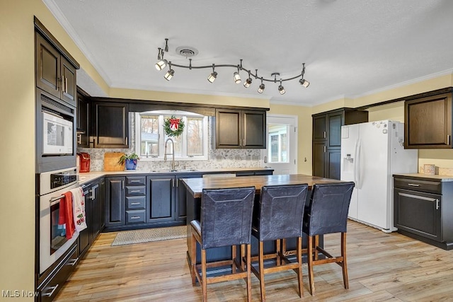 kitchen featuring a center island, white appliances, sink, light wood-type flooring, and ornamental molding