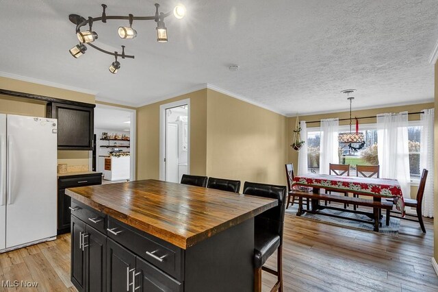 kitchen featuring a center island, hanging light fixtures, white fridge, light hardwood / wood-style floors, and a breakfast bar area