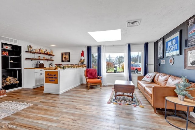 living room with a skylight, a textured ceiling, and light wood-type flooring