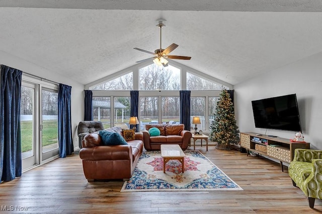 living room with ceiling fan, high vaulted ceiling, light hardwood / wood-style floors, and a textured ceiling