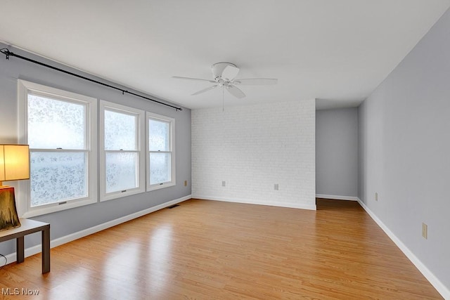 unfurnished room with ceiling fan, light hardwood / wood-style floors, and brick wall