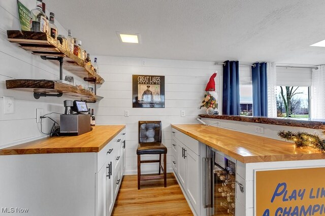 bar with wood counters, light wood-type flooring, white cabinetry, and wine cooler