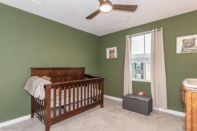 bedroom with a crib, light carpet, and ceiling fan