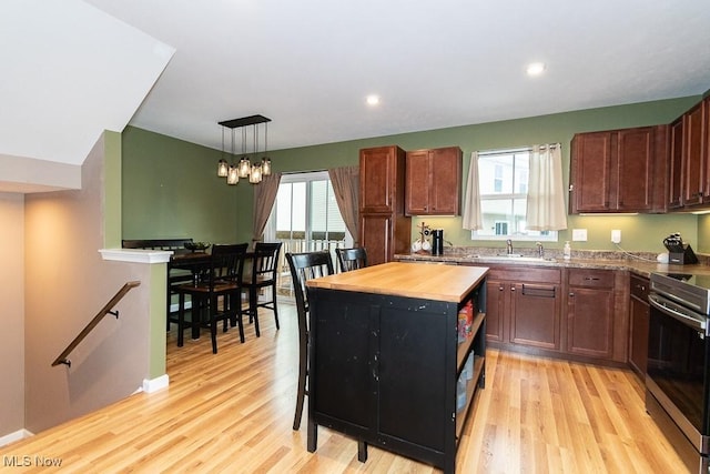 kitchen featuring light wood-type flooring, decorative light fixtures, a healthy amount of sunlight, and stainless steel range oven