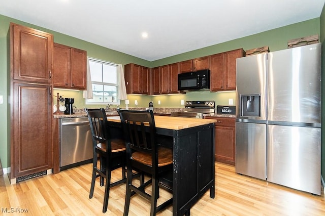 kitchen with light hardwood / wood-style floors, a kitchen island, a kitchen bar, and appliances with stainless steel finishes