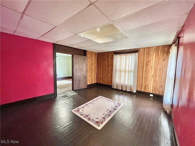 empty room featuring dark hardwood / wood-style floors, wood walls, and a drop ceiling