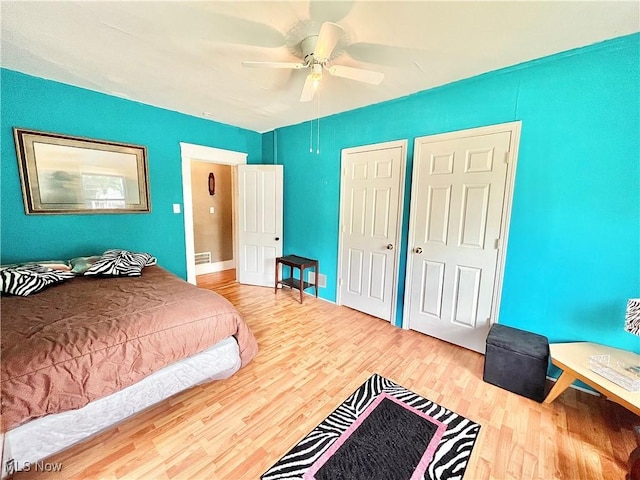 bedroom featuring ceiling fan, wood-type flooring, and multiple closets