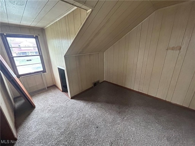 additional living space with wooden walls, light colored carpet, and vaulted ceiling