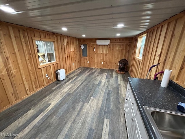 basement with wooden walls, a wall mounted AC, dark wood-type flooring, and sink