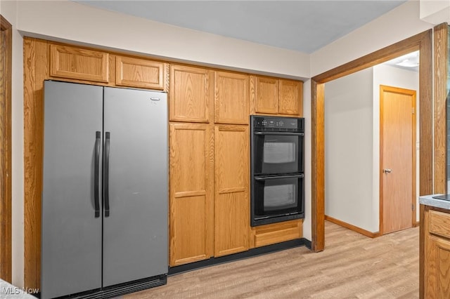 kitchen featuring stainless steel fridge, light wood-type flooring, and black double oven