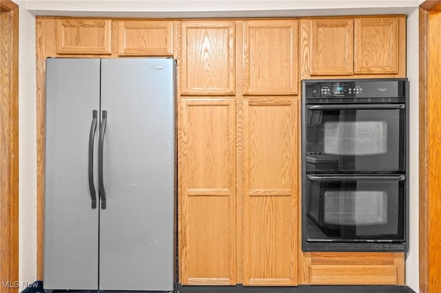 kitchen with double oven, light brown cabinetry, and stainless steel refrigerator