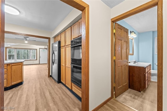 kitchen with stainless steel fridge, light wood-type flooring, double oven, and sink