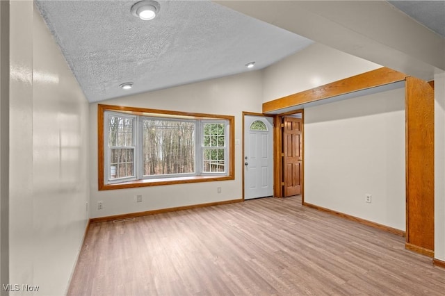 interior space featuring a textured ceiling, light wood-type flooring, and vaulted ceiling