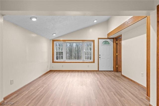 interior space featuring light wood-type flooring, lofted ceiling, and a textured ceiling