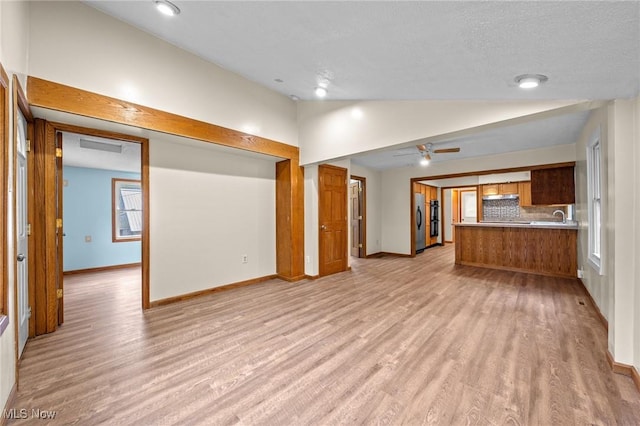 unfurnished living room with a textured ceiling, ceiling fan, light hardwood / wood-style floors, and lofted ceiling