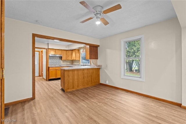 kitchen featuring kitchen peninsula, light wood-type flooring, backsplash, a textured ceiling, and ceiling fan