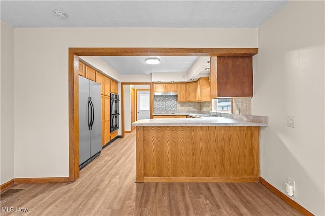 kitchen featuring kitchen peninsula, light wood-type flooring, stainless steel refrigerator, and backsplash