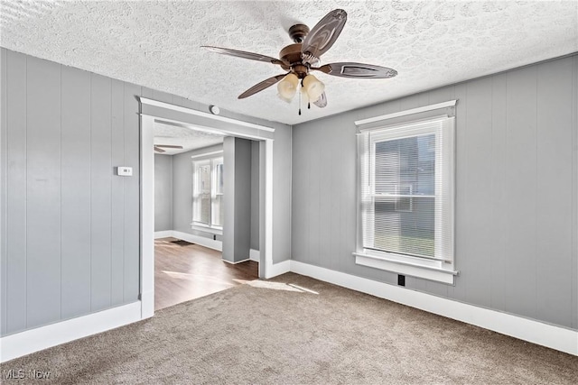 spare room featuring a textured ceiling, carpet floors, ceiling fan, and wood walls